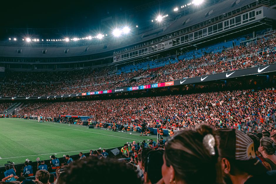 Packed football stadium under night lights with a cheering crowd and green field.