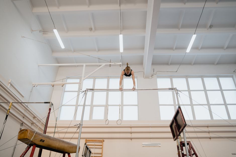 Young female gymnast skillfully practicing on uneven bars in a bright gym setting.